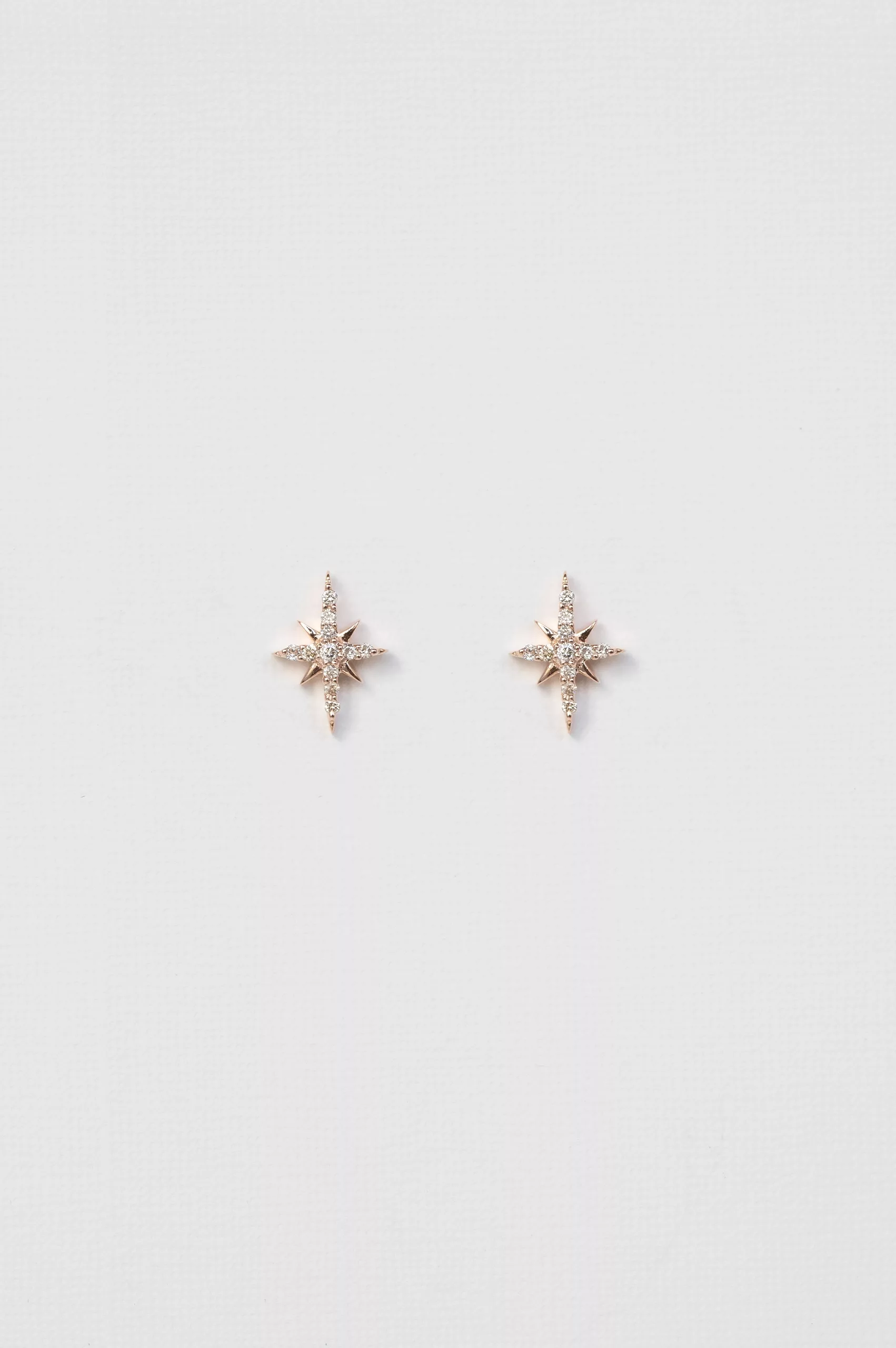 rose gold stud earrings each featuring an eight-pointed north star set with round brilliant diamonds at the center