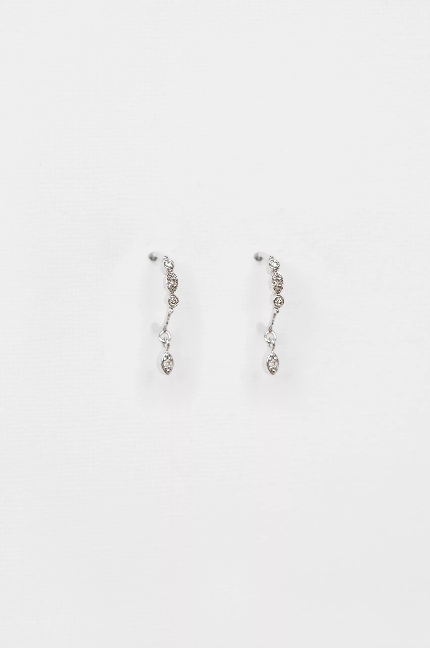 white gold drop earrings each featuring a vertical cascade of three bezel-set diamonds with a smaller dangling diamond at the base
