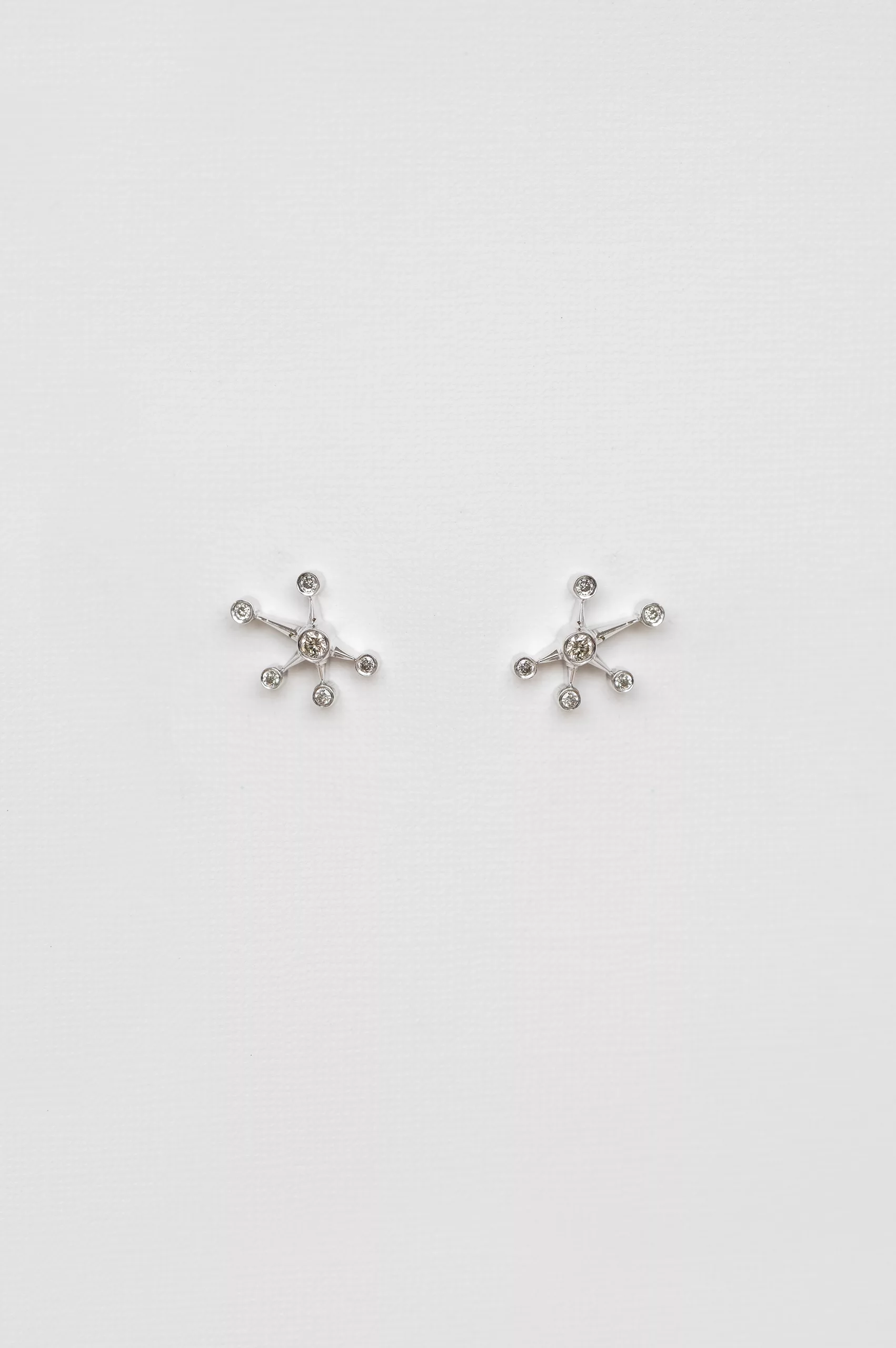 white gold stud earrings each shaped as a starburst with six radiating arms tipped with round diamonds, evoking a constellation pattern