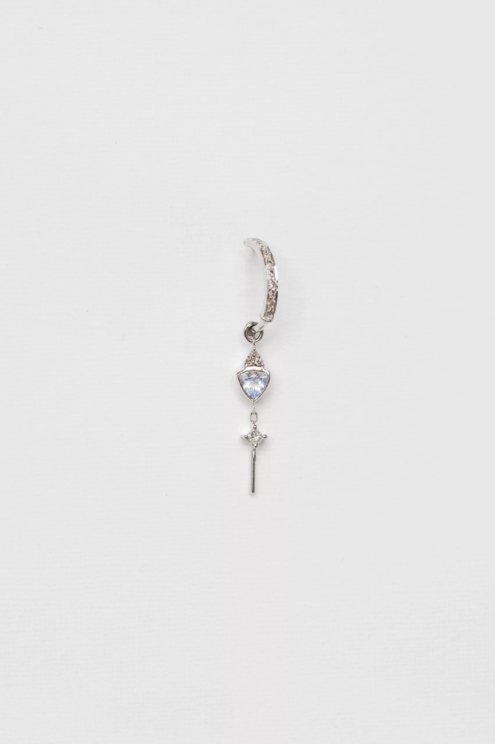 white gold single hoop earring with a pavé diamond hoop suspending a triangular moonstone and a small diamond cross charm